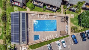 An aerial view of a residential area with a swimming pool, solar panels, and parked cars. - Beautiful Ocean View 2 Bedroom Condo 1 Min Walk to Beach! (Kihei)