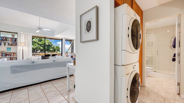 Ein moderner Waschraum mit Waschmaschine und Trockner, ein großes Fenster mit Blick auf Grünflächen sowie eine Sitzecke mit Sofa und Bücherregalen.