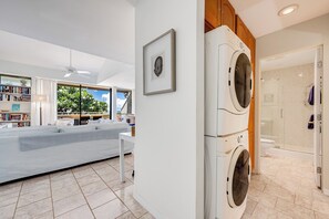 Een moderne wasruimte met een wasmachine en droger, een groot raam met uitzicht op groen, en een zithoek met een bank en boekenkasten.