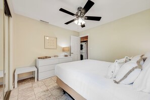 Een slaapkamer met een bed, een plafondventilator, een dressoir, een nachtkastje en een wasmachine op de achtergrond.
