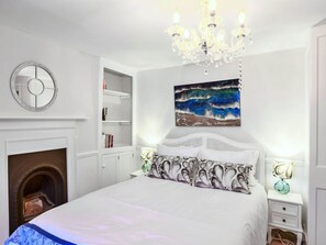 A bedroom with a white bed, a fireplace, a chandelier, a painting, and a round mirror. - Holiday Stay With Sea Glimpse (Torpoint)