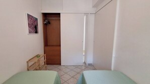 A small, clean room with two beds, a wooden wardrobe, and a door leading to another room. - The Residences 3 (Marina di Modica)