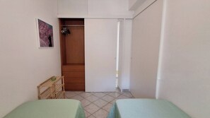 Ein kleiner, sauberer Raum mit zwei Betten, einem Holzschrank und einer Tür zu einem weiteren Zimmer.