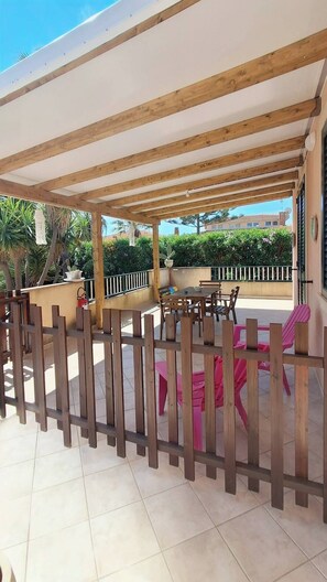 Eine Terrasse im Freien mit einer Holz-Pergola, Fliesenboden und einer Sitzecke mit Stühlen und einem Tisch.
