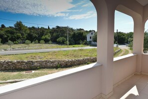 Un balcone con un muro in pietra e vista su una strada che porta a un edificio bianco in lontananza.