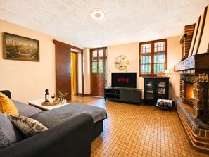 A living room with a fireplace, a television, and a sofa. - Family home in a green setting with a large, wooded lot (Rai)