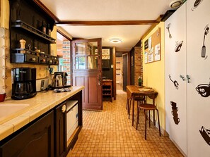 A kitchen with a coffee maker, a dining table with chairs, and a refrigerator with cartoon cutlery decals. - Family home in a green setting with a large, wooded lot (Rai)