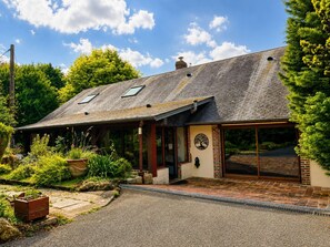 A house with a sloped roof, a covered porch, and a brick exterior. - Family home in a green setting with a large, wooded lot (Rai)