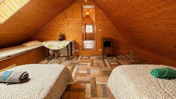 Un dormitorio abrigado en un ático con paredes de madera, techo inclinado, una mesita y dos camas.
