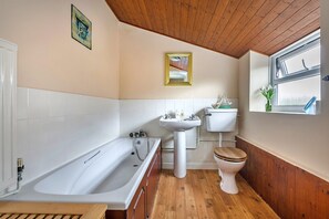 A bathroom with a bathtub, sink, toilet, wooden floor, and a window with a view. - Family Home With Sea Views (Cromer)