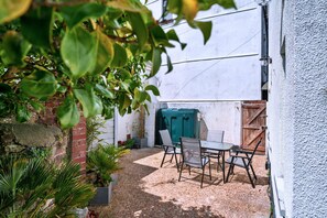 Eine Terrasse mit Tisch und Stühlen, umgeben von Pflanzen und einer Backsteinmauer.