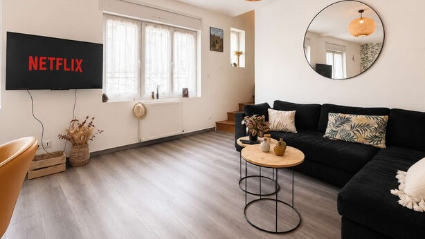 Una sala de estar moderna con un sofá negro, una mesa redonda de centro y un televisor de pantalla plana mostrando 'NETFLIX'.