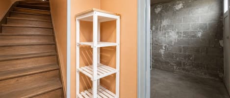 Un coin avec une étagère blanche, un escalier en bois et un mur en briques.