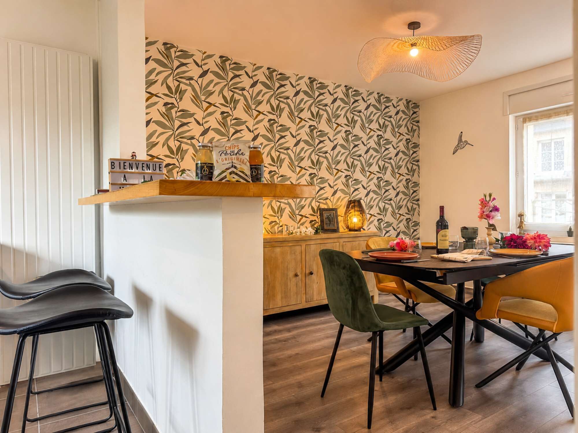 Ein Essbereich mit einem Holztisch, Stühlen und einer Wand mit einem Blättermotiv.
