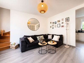 A modern living room with a black sofa, two side tables, a round mirror, and a wooden floor. - 2-bedroom apartment, 2 bathrooms, garage, and greenway (Alençon)