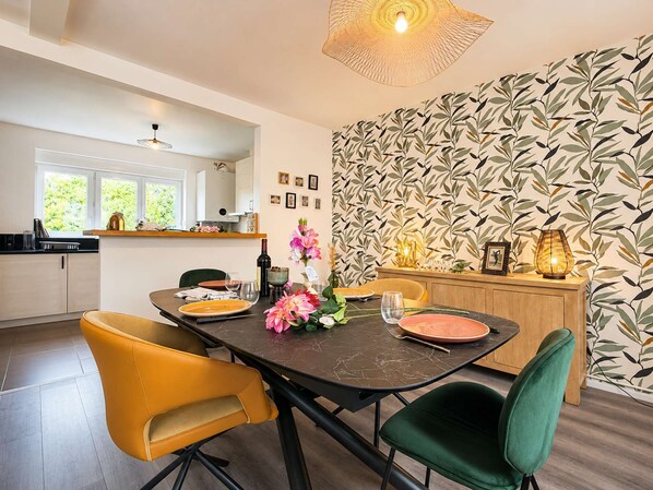 A modern dining area with a dark marble table, yellow and green chairs, and a patterned wallpaper.