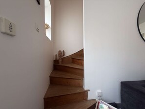 Eine Treppe mit Holzhufen, die nach oben führt, ein an der Wand befestigter Lichtschalter und ein kleines Fenster für natürliches Licht.