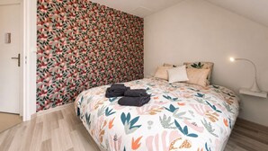 Un dormitorio con papel tapiz floral, una cama con colcha estampada y una lámpara de noche.