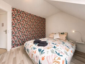Ein Schlafzimmer mit floralem Wandpapier, einem Bett mit gemustertem Überwurf und einer Nachttischlampe.