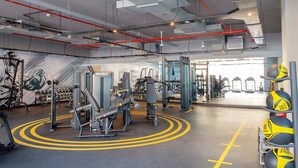 Een fitnessruimte met trainingsapparatuur, gele lijnen op de vloer en een rek met medicine balls.