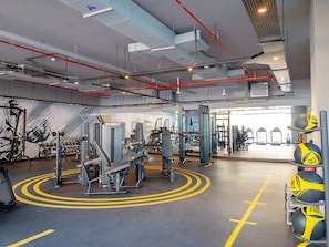 Ein Fitnessraum mit Trainingsgeräten, gelben Linien auf dem Boden und einem Medizinballregal.