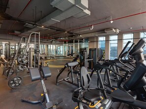 Ein Fitnessstudio mit unterschiedlichen Trainingsgeräten, großen Fenstern und einer hohen Decke.