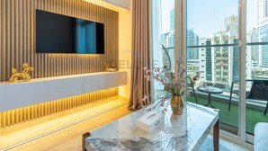 Een moderne hotelkamer met een grote televisie bevestigd aan een houten wandpaneel, een marmeren receptiebalie en een balkon met uitzicht op de stadsgezicht.