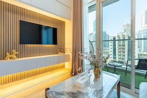 Ein modernes Hotelzimmer mit einem großen Fernseher, der an einer Wand aus Holzpaneelen befestigt ist, einem мраморном Empfangstresen und einem Balkon mit Blick auf die Stadt.