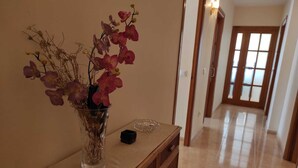 A hallway with a vase of flowers on a table, a door with frosted glass panels, and a light fixture on the wall. - Beachfront Apartment (S'Arenal)