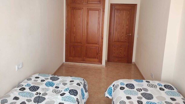 A room with two beds, a large wooden wardrobe, and a plain wall. - Beachfront Apartment (S'Arenal)