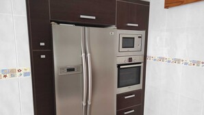 A kitchen with a stainless steel refrigerator, a microwave, and an oven built into a dark cabinetry unit. - Beachfront Apartment (S'Arenal)