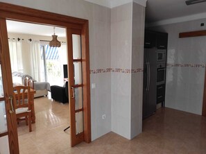 Une pièce avec une porte en bois, un lit, une chaise et un coin cuisine équipé d’un réfrigérateur.