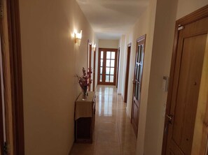 A hallway with a wooden door on the right, a light fixture on the left, and a vase with flowers on a table.