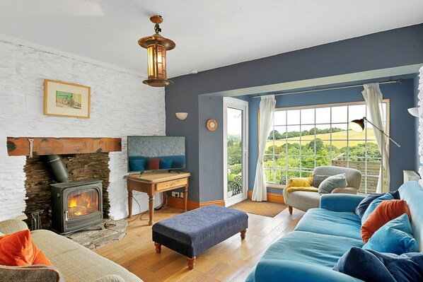 A cozy living room with a stone fireplace, a television, and a large window with a view of greenery. - Haven Near Dartmouth Ferry (Dartmouth)