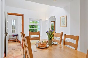 A dining area with a wooden table, chairs, a vase with flowers, and a plate of croissants. - Haven Near Dartmouth Ferry (Dartmouth)