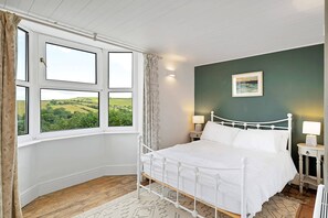 A bedroom with a bed, a nightstand, a lamp, and a view of the countryside through a window. - Haven Near Dartmouth Ferry (Dartmouth)