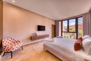 Habitación de hotel con cama, televisor montado en la pared, una silla y ventana con vistas al exterior.
