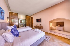 A hotel room with a large bed, a seating area, a television, and a bathroom visible through an open door. - Riad Majorelle – Al Maaden Golf – Marrakech (Marrakech)