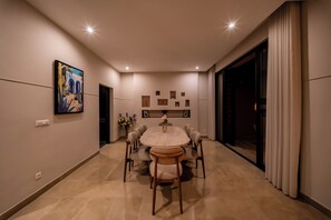 A modern dining room with a round table, six chairs, and a large painting on the wall. - Riad Majorelle – Al Maaden Golf – Marrakech (Marrakech)