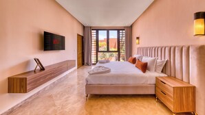 Ein Hotelzimmer mit einem großen Bett, einem an der Wand befestigten Fernseher, einem Nachttisch aus Holz und Blick ins Freie durch das Fenster.