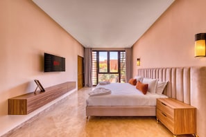 A hotel room with a large bed, a TV mounted on the wall, a wooden bedside table, and a view of the outdoors through the window. - Riad Majorelle – Al Maaden Golf – Marrakech (Marrakech)