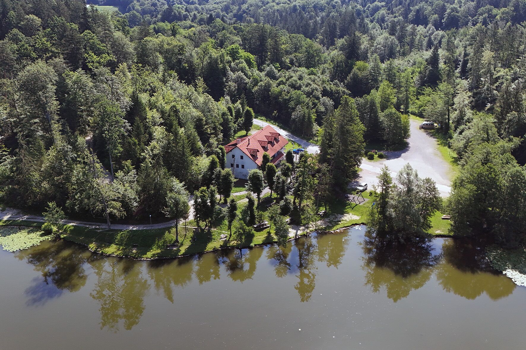 Une maison entourée d’une forêt dense et bordée par un plan d’eau.