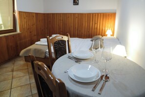 Un comedor con una mesa redonda para dos personas, una cama con cabecera de madera al fondo y una ventana con persianas.