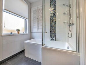 A bathroom with a bathtub, a shower, and a window with decorative items. - Victorian Caernarfon House for 6 (Caernarfon)