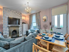 A living room with a fireplace, sofa, television, and dining area with a table set for two. - Victorian Caernarfon House for 6 (Caernarfon)