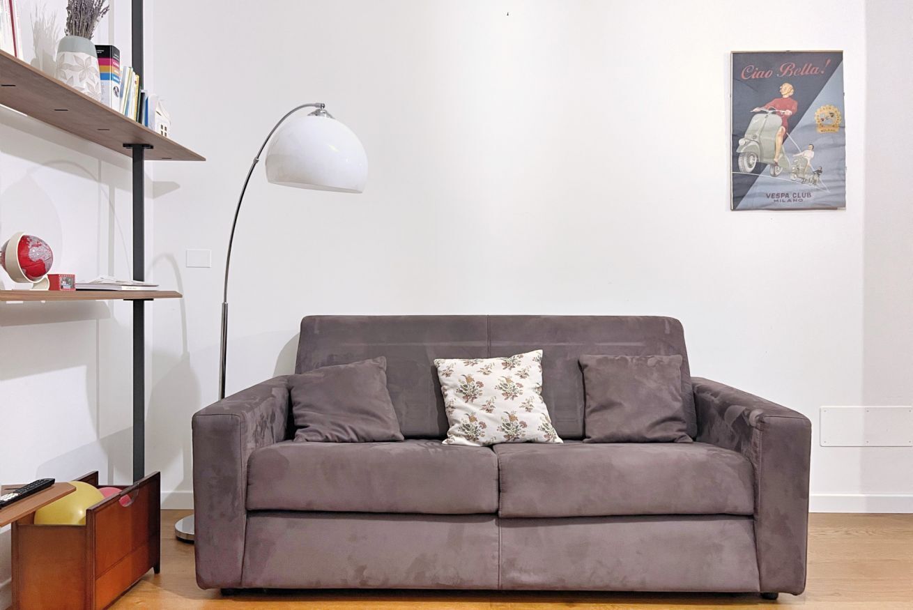 A grey sofa with floral cushions, a floor lamp, and a poster on the wall.