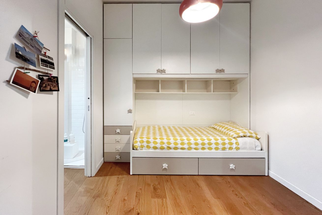 Quarto com cama, espaço de armazenamento embutido, guarda-roupa e porta para uma casa de banho.