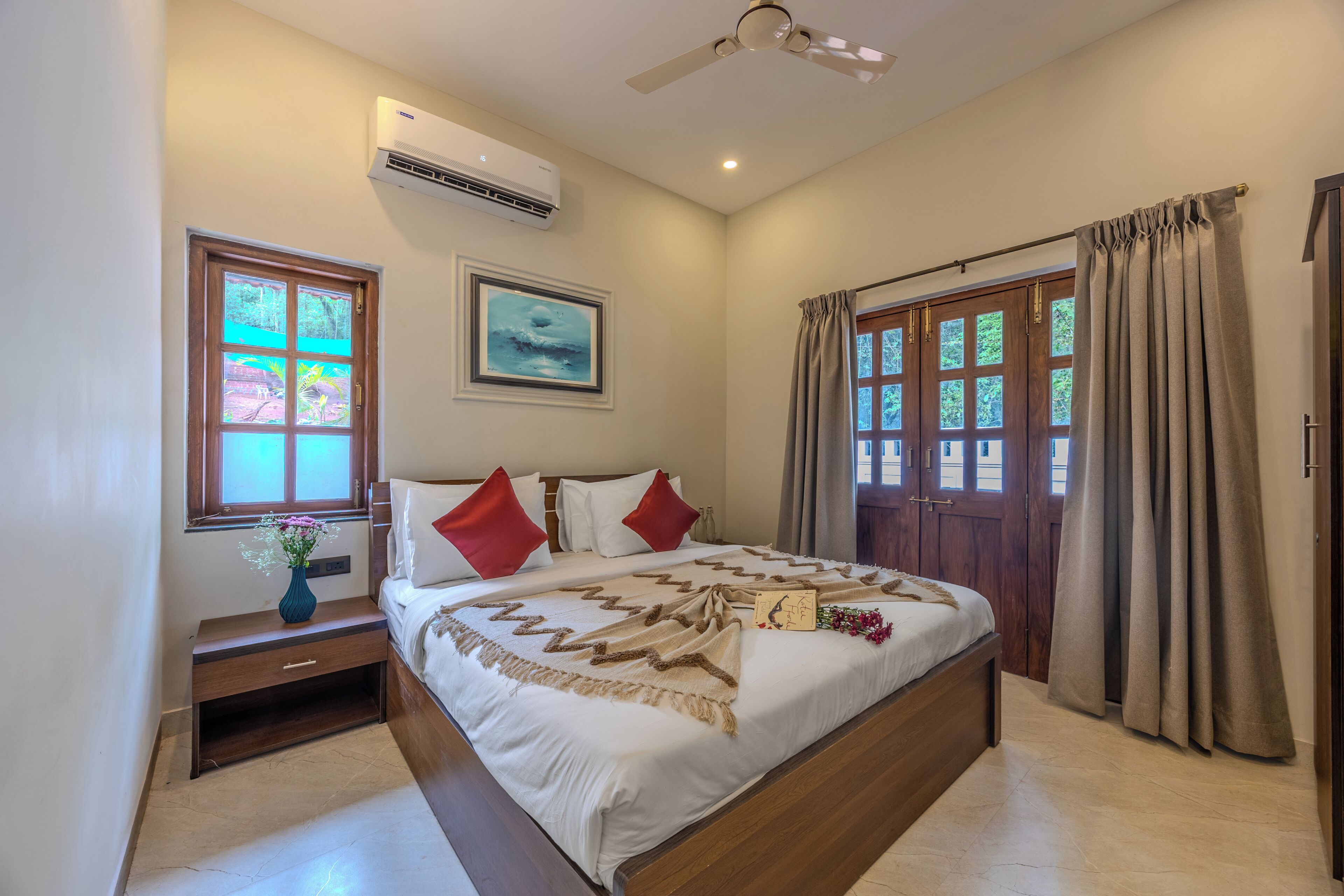 Un dormitorio con cama, mesita de noche, ventana con cortinas, ventilador de techo y aire acondicionado.