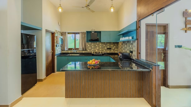A modern kitchen with a central island, a built-in oven, and a ceiling fan. - ELIVAAS Casa Vilson 3BHK Villa with Pool (Salvador du Mundu)
