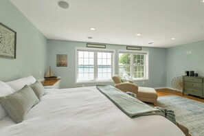 A bedroom with a large bed, a chair, a dresser, and a view of the outdoors. - NEW FOR 2027 Lake Winnipesaukee Waterfront Sleeps 16 (Moultonborough)